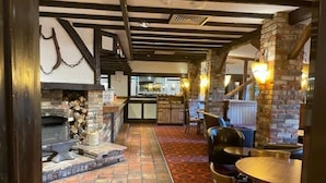 A cozy pub with exposed wooden beams, a stone fireplace, and a red patterned carpet. - Living The Dream (Holt)