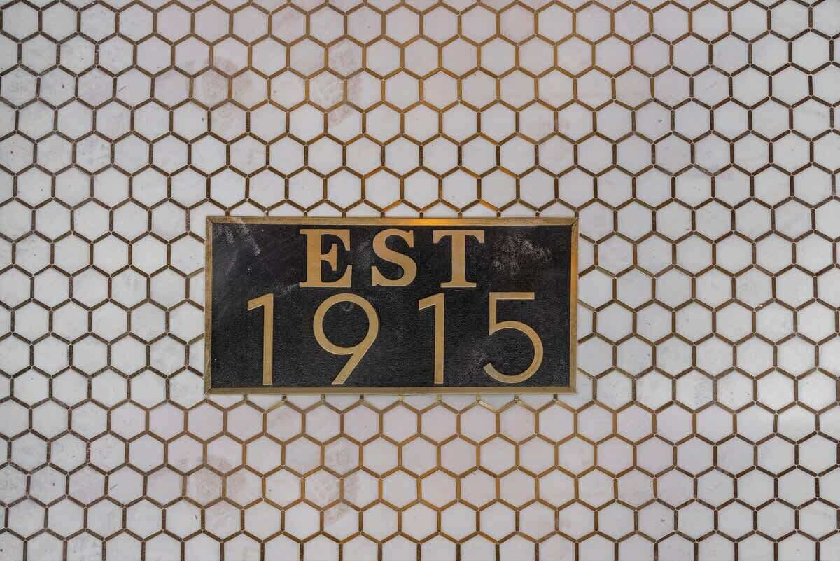 A sign with the text "EST 1915" on a hexagonal tile background.