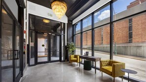 A modern lobby with a chandelier, a glass door entrance, and a seating area with yellow chairs and a table. - Park Hotel 1BR Suite 310 (Chattanooga)