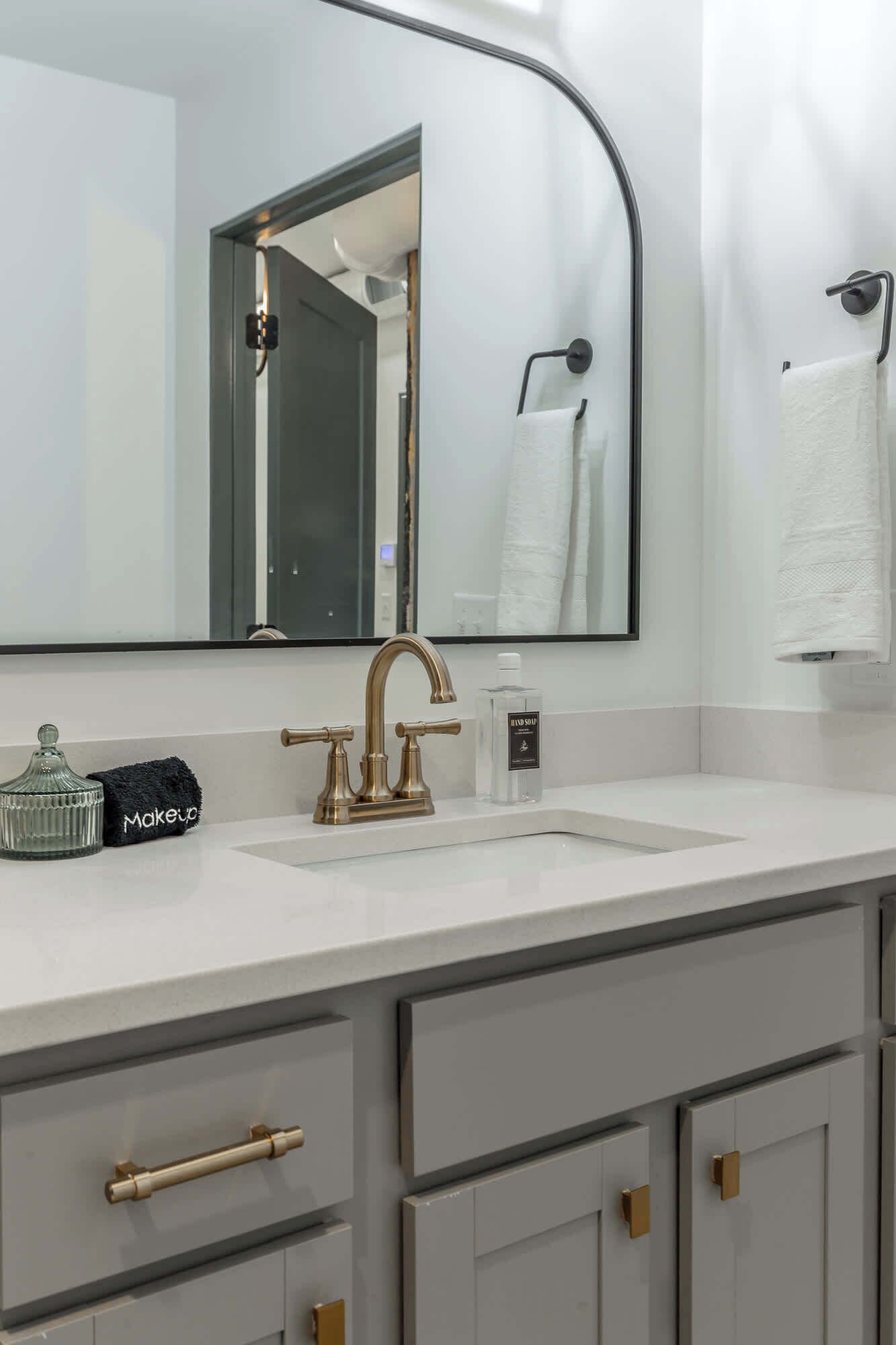 Une salle de bain avec un lavabo blanc, un robinet doré et un miroir muni d’un porte-serviettes. On y trouve deux tiroirs et un meuble sous le lavabo.