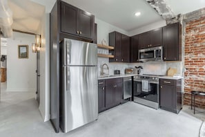 A modern kitchen with stainless steel appliances, dark cabinetry, and a brick accent wall. - Park Hotel 2BR Suite 406 (Chattanooga)