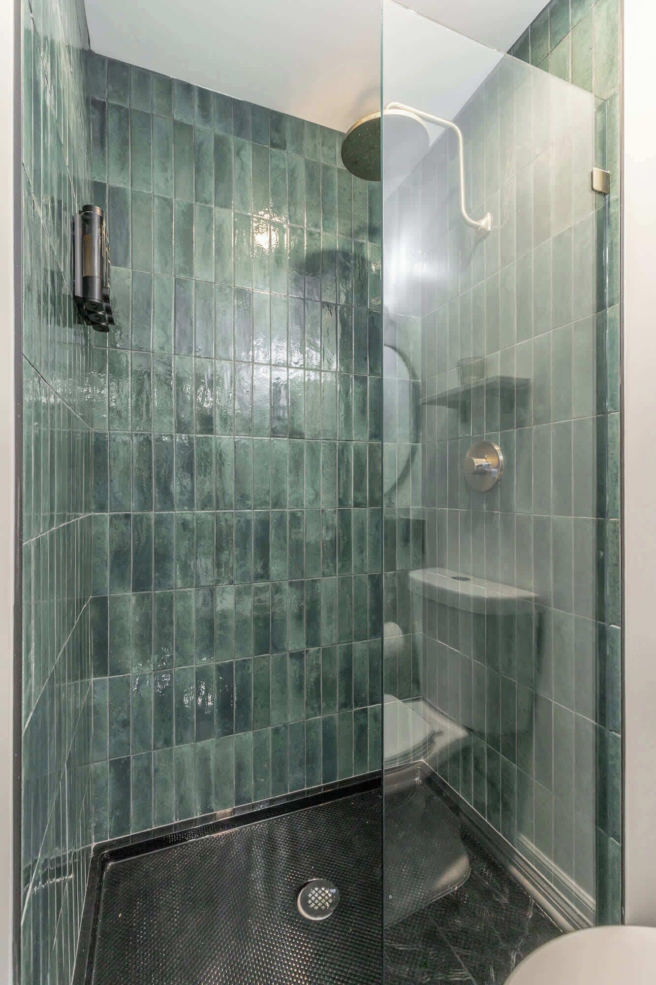 Cabina doccia in vetro con soffione a mano e rubinetto a parete.