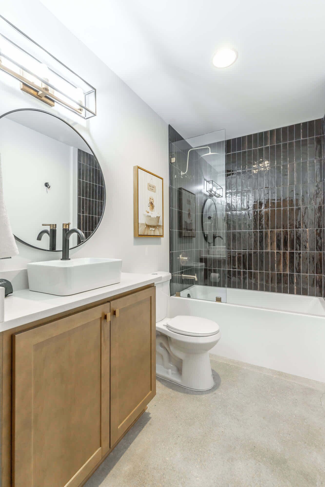 A modern bathroom with a white vanity, a large mirror, a framed picture, a glass shower enclosure, and a white toilet.