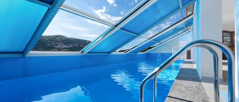 Una piscina azul cristalina con una escalera metálica que da al agua, rodeada por una estructura arquitectónica moderna con grandes ventanales.