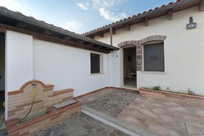A building with a stone patio, a brick fireplace, and a door leading to an interior space. - Villa Nuragica - Deluxe Apartment (Nuraxi Figus)