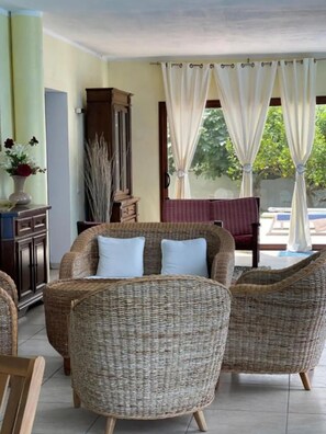 A room with wicker furniture, a cabinet, and a view of greenery outside. - Villa Nuragica - Deluxe Apartment (Nuraxi Figus)