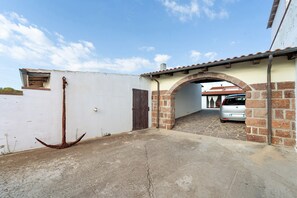 Un callejón estrecho con un ancla rústica, una pared blanca y un arco de ladrillo que da a un coche estacionado.