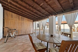 An outdoor patio with a round table and chairs, a bicycle, and a bamboo wall. - Villa Nuragica - Deluxe Apartment (Nuraxi Figus)