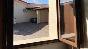 An open window with a view of a building's exterior, including a car parked in a covered area. - Villa Nuragica - Classic Apartment (Nuraxi Figus)