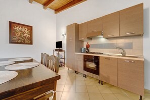 A modern kitchen with wooden cabinets, a built-in oven, and a dining area with a table and chairs. - Villa Nuragica - Classic Apartment (Nuraxi Figus)