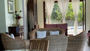 A dining area with wicker furniture, a glass table, and a view of the outdoors. - Villa Nuragica - Classic Apartment (Nuraxi Figus)