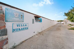 Un chemin menant à la Villa Nuragica, avec des panneaux indiquant son nom.