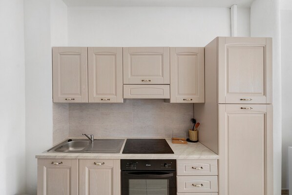 A kitchen with light-colored cabinets, a stainless steel sink, a black stove, and a built-in oven.