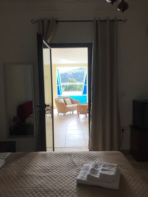 Ein Schlafzimmer mit einem Bett, einem Fenster und Blick auf einen Außenbereich mit Stuhl und Tisch.