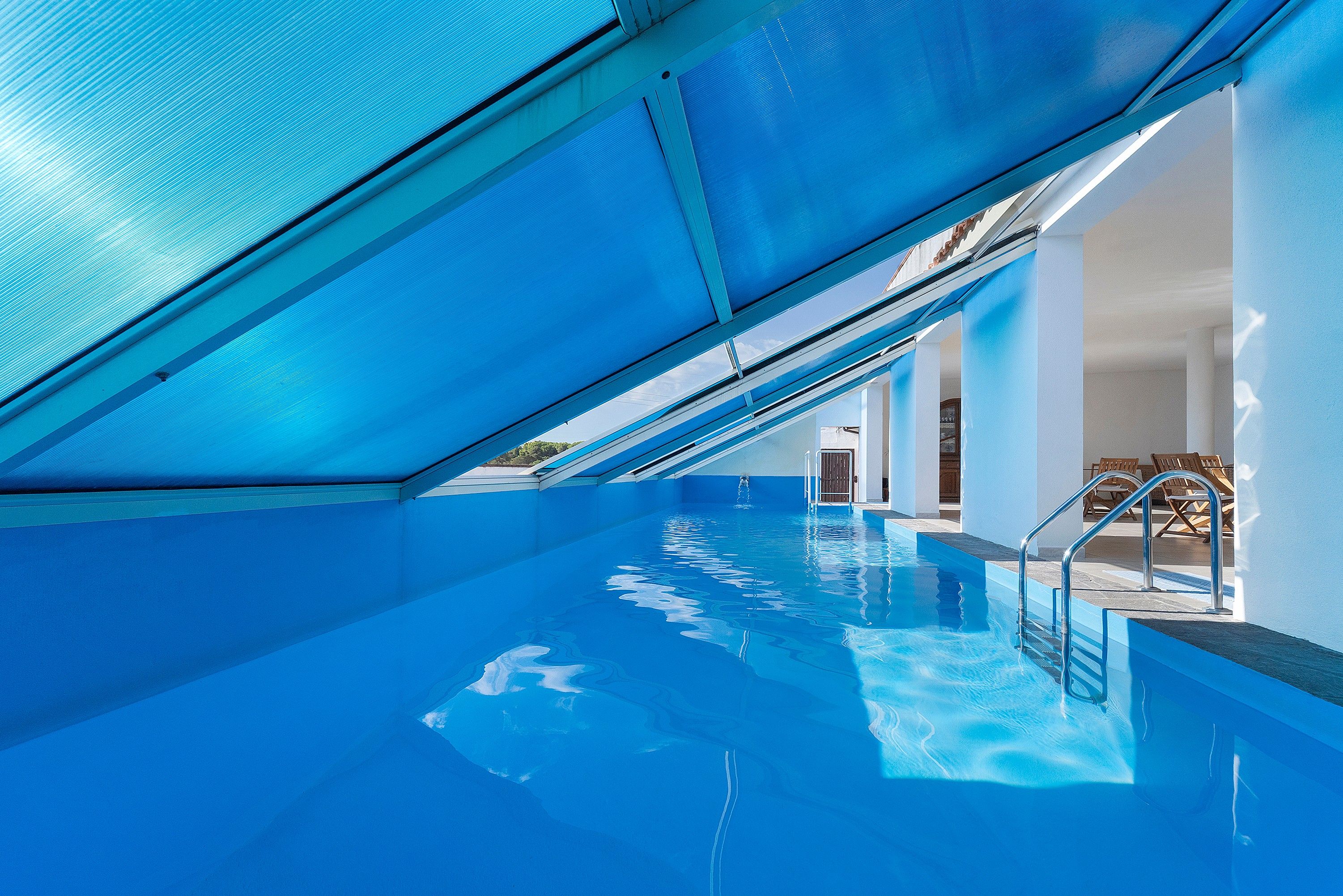 Una piscina interior con agua azul cristalina, techo inclinado y vista al espacio interior.