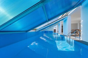 Une piscine intérieure à l’eau d’un bleu cristallin, dotée d’un plafond incliné et offrant une vue sur l’espace intérieur.