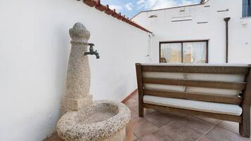 Un bagno esterno in pietra con un rubinetto, una panca di legno e un edificio bianco con tetto in tegole.