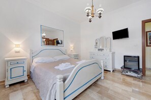 Ein Schlafzimmer mit einem Bett, Nachttischen, einem Fernseher, einem Spiegel und einer Kandelaber.