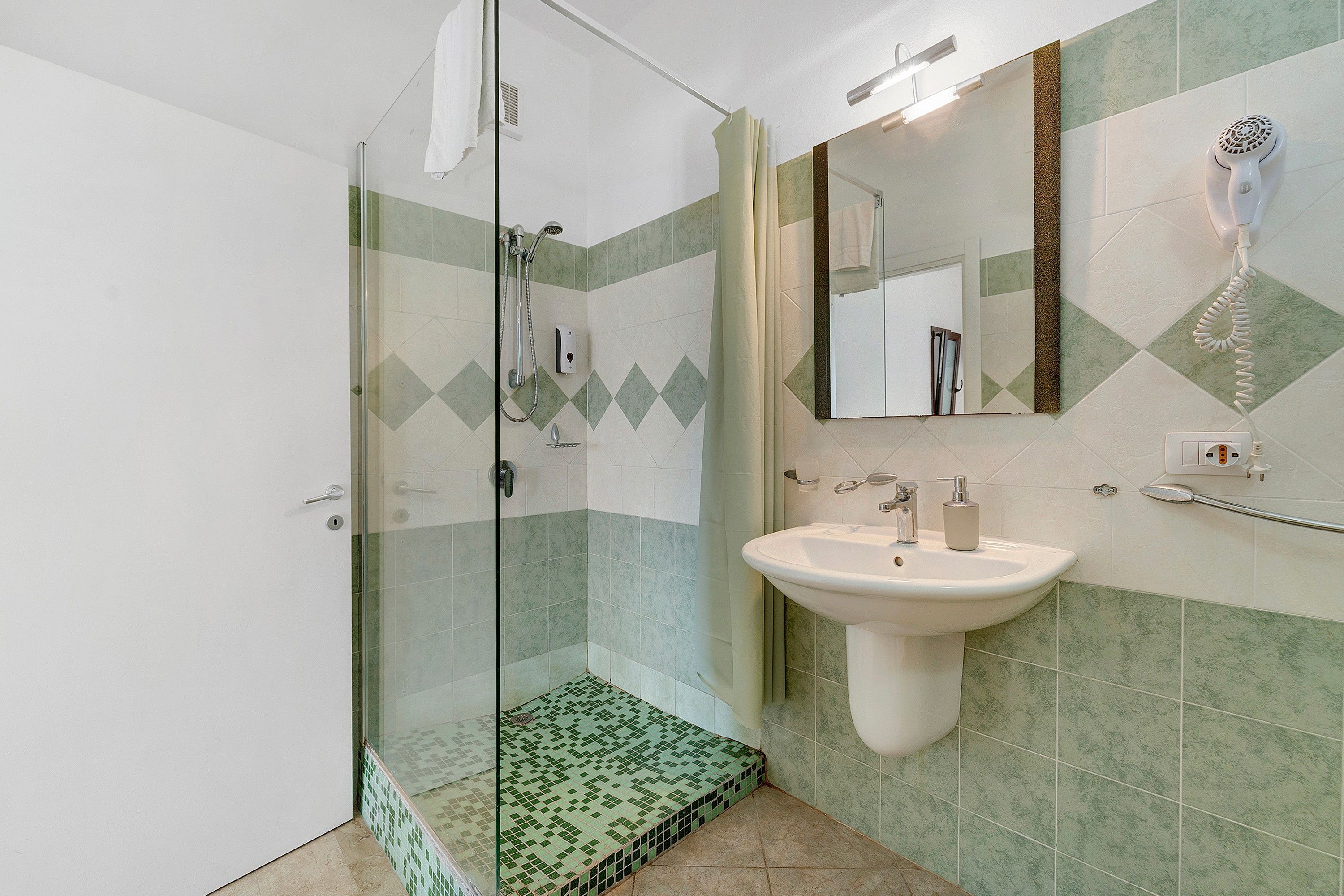 A bathroom with a glass-enclosed shower, a sink with a mirror, and patterned tiles.