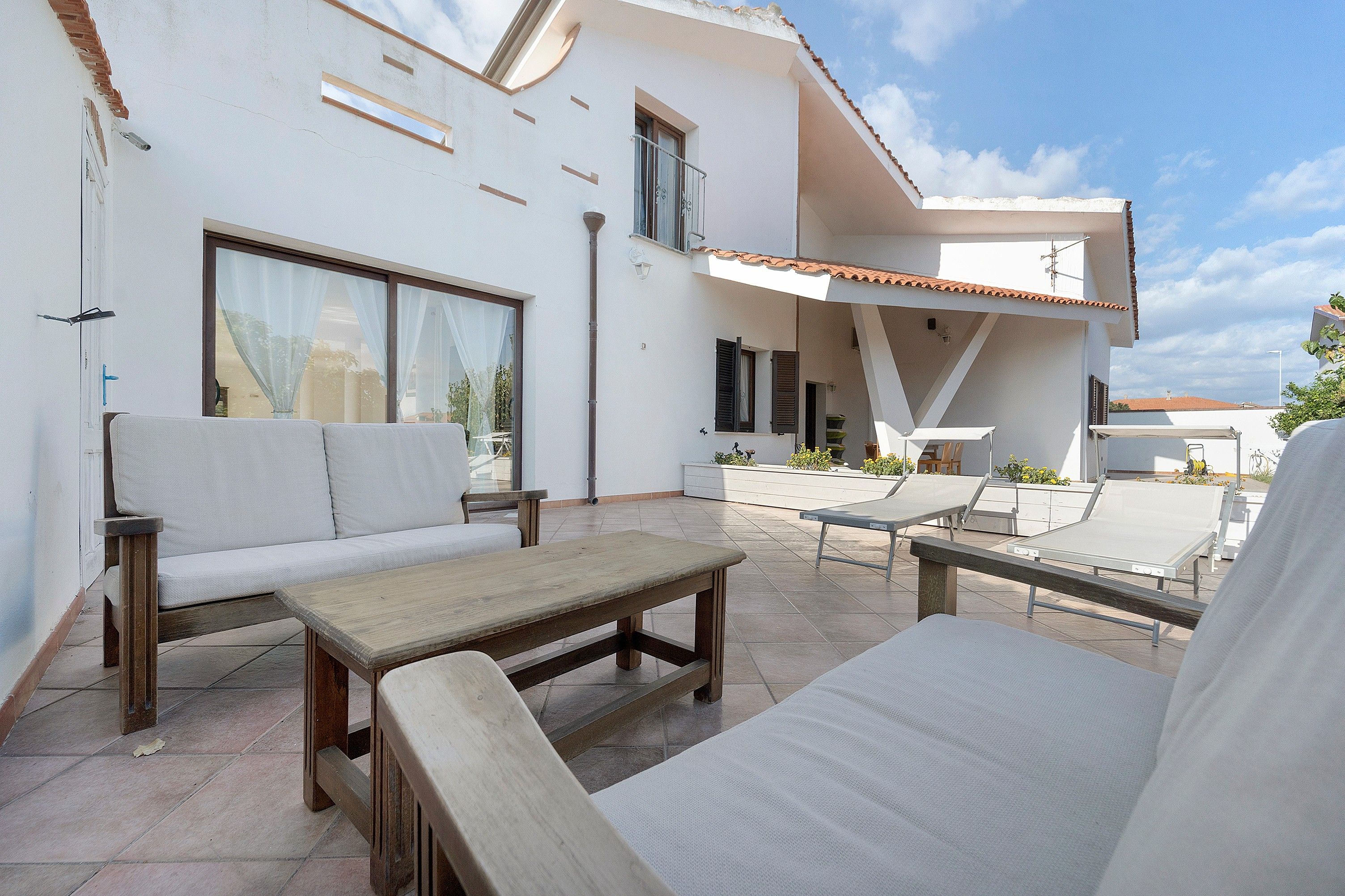 Een modern terras buiten met een bank, een houten tafel en een lounge stoel.