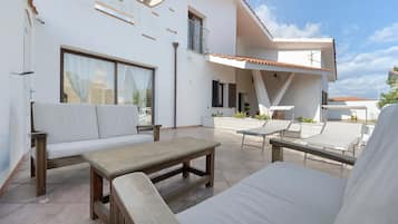 Een modern terras buiten met een bank, een houten tafel en een lounge stoel.
