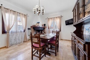 A dining area with a wooden table, chairs, a chandelier, and a fireplace. - Villa Nuragica - Apartment with Garden (Nuraxi Figus)