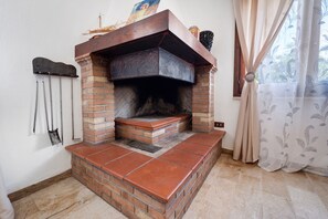A brick fireplace with a chimney, a hanging coat rack, and a window with curtains. - Villa Nuragica - Apartment with Garden (Nuraxi Figus)