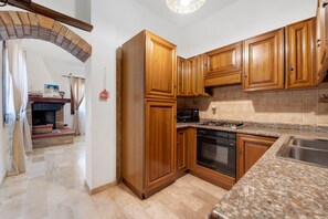 A kitchen with wooden cabinets, a built-in oven, a microwave, and a granite countertop. - Villa Nuragica - Apartment with Garden (Nuraxi Figus)