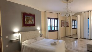 Une chambre à coucher avec un lit, des lampes de chevet, un lustre, un miroir et des œuvres d’art accrochées au mur.