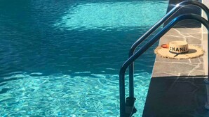 A clear indoor pool with a blue and white color scheme, a metal ladder, and a Chanel hat on the edge.