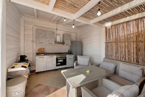 Een praktische keuken met een inbouwoven, een klein eethoekje met een tafel met glazen blad, en een rieten bank.