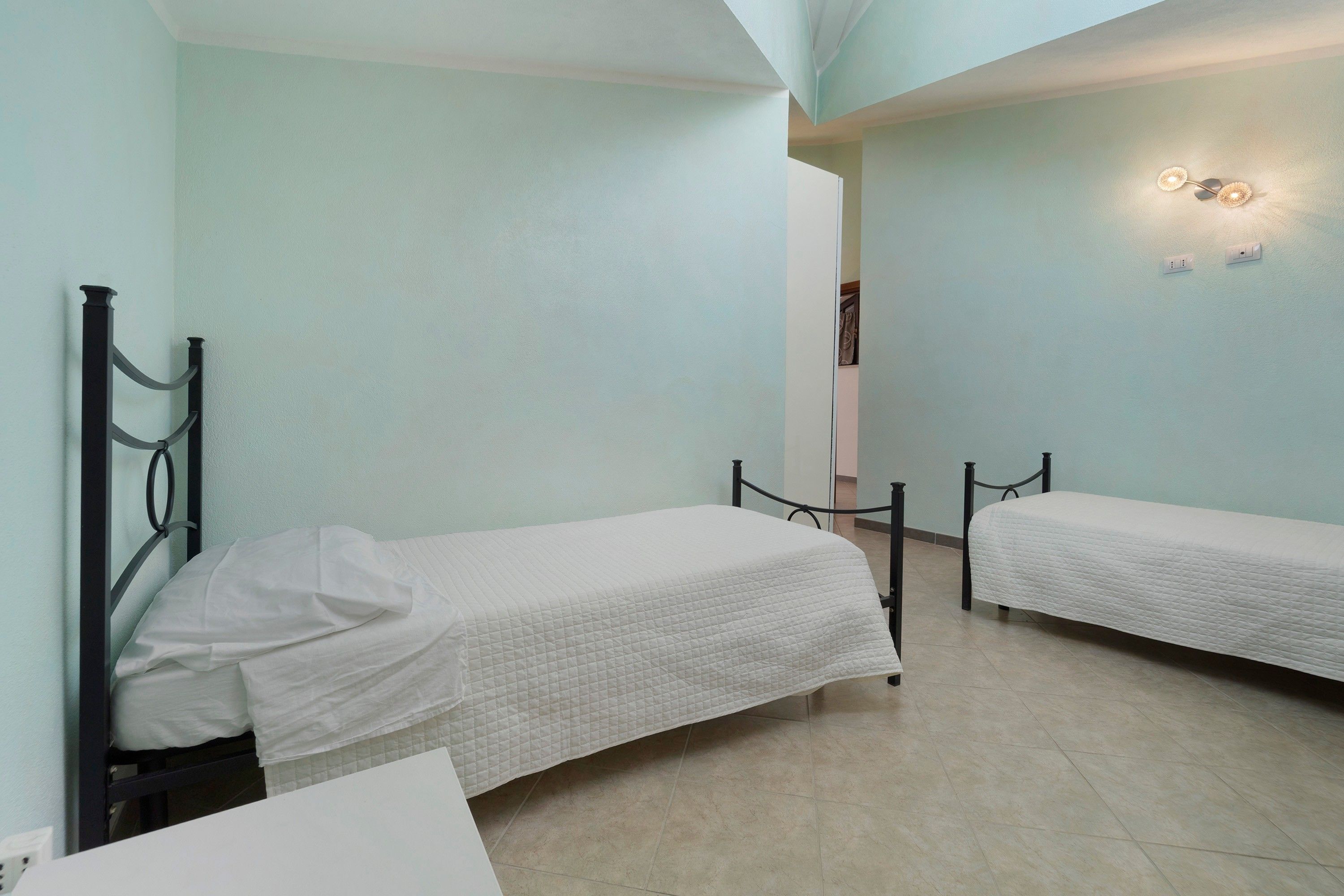 A room with two single beds, a white wall, and a ceiling light fixture.