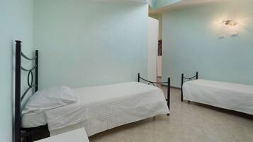 A room with two single beds, a white wall, and a ceiling light fixture.