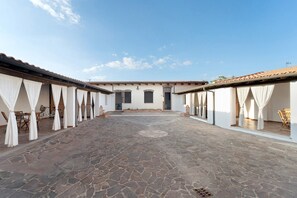 A courtyard with stone flooring, white walls, and tiled roofs. There are two doors and a window visible.