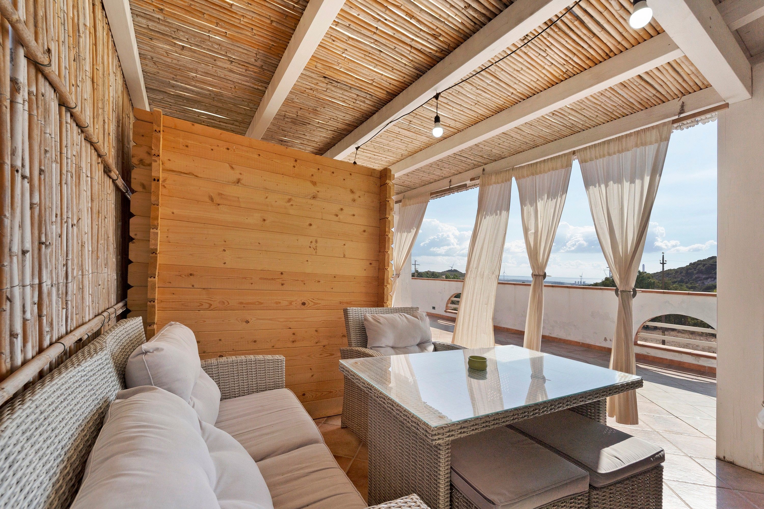 Ein sonnendurchflutetes Zimmer mit Holzbalkendecke, einem Sofa, einem Tisch und Blick auf die Landschaft.