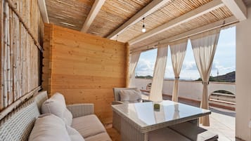 Ein sonnendurchflutetes Zimmer mit Holzbalkendecke, einem Sofa, einem Tisch und Blick auf die Landschaft.