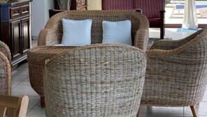 A room with wicker furniture, a cabinet, and a view of greenery outside.