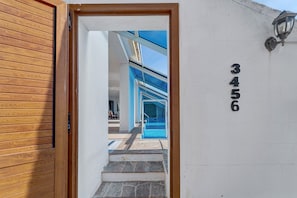 A wooden door leading to a pool area with a clear sky above.