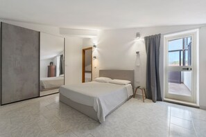 Een moderne slaapkamer met een groot bed, een kledingkast, een spiegel en een schuifdeur naar een balkon.