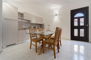 A modern kitchen with a dining table and chairs, a microwave, and a black door with windows. - Villa Nuragica - Apartment (Nuraxi Figus)