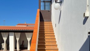 Eine Treppe führt zu einer Tür mit Glasscheibe, im Hintergrund eine weiße Wand und ein Ziegeldach.