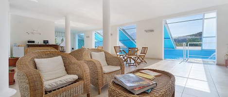 A spacious living area with wicker furniture, a dining set, and a view of the sea.