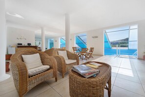 Amplia sala de estar con mobiliario de mimbre, comedor y vista al mar.