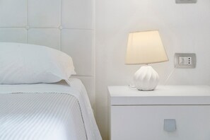 Una cama bien hecha con un cabecero blanco y una mesita de noche con una lámpara.