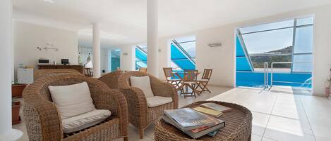 A spacious living area with wicker furniture, a dining set, and a view of a pool.