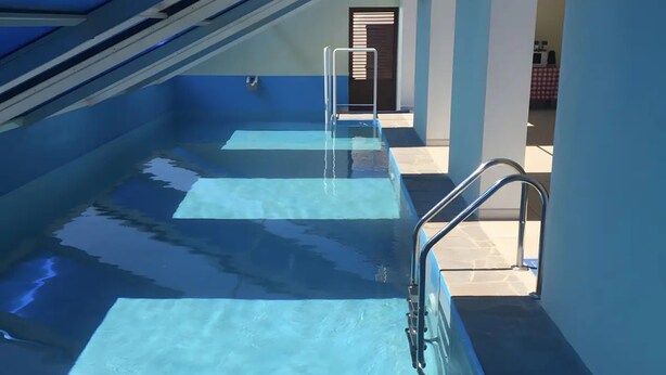 A swimming pool with a glass floor, metal railings, and a view of the interior. - Villa Nuragica – Room with Private Bathroom (Nuraxi Figus)