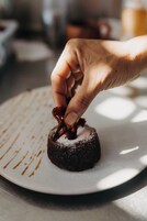 A hand holding a piece of chocolate with a dusting of powdered sugar on a plate.