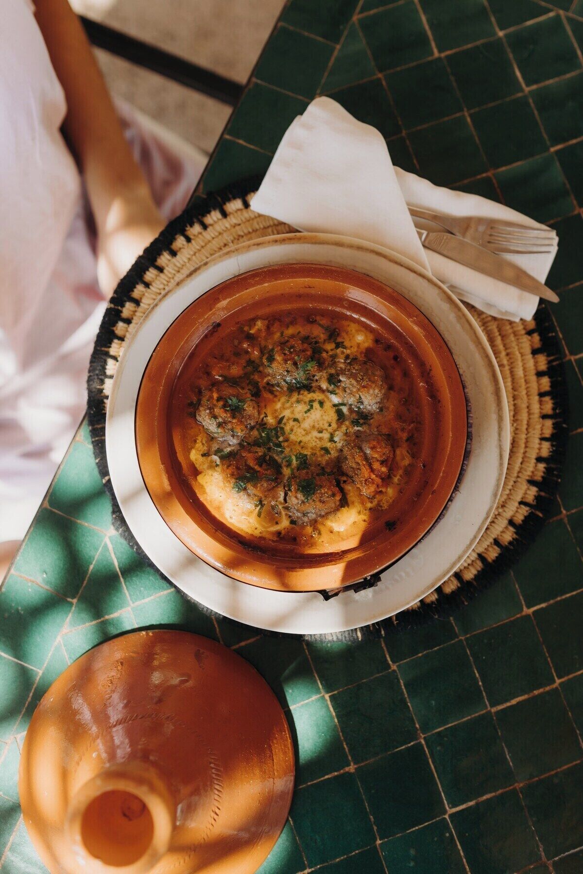 A bowl of soup with meatballs on a plate, placed on a table with a woven placemat.