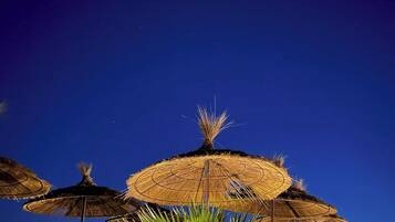 A night scene with thatched umbrellas and lounge chairs, suggesting a resort setting.