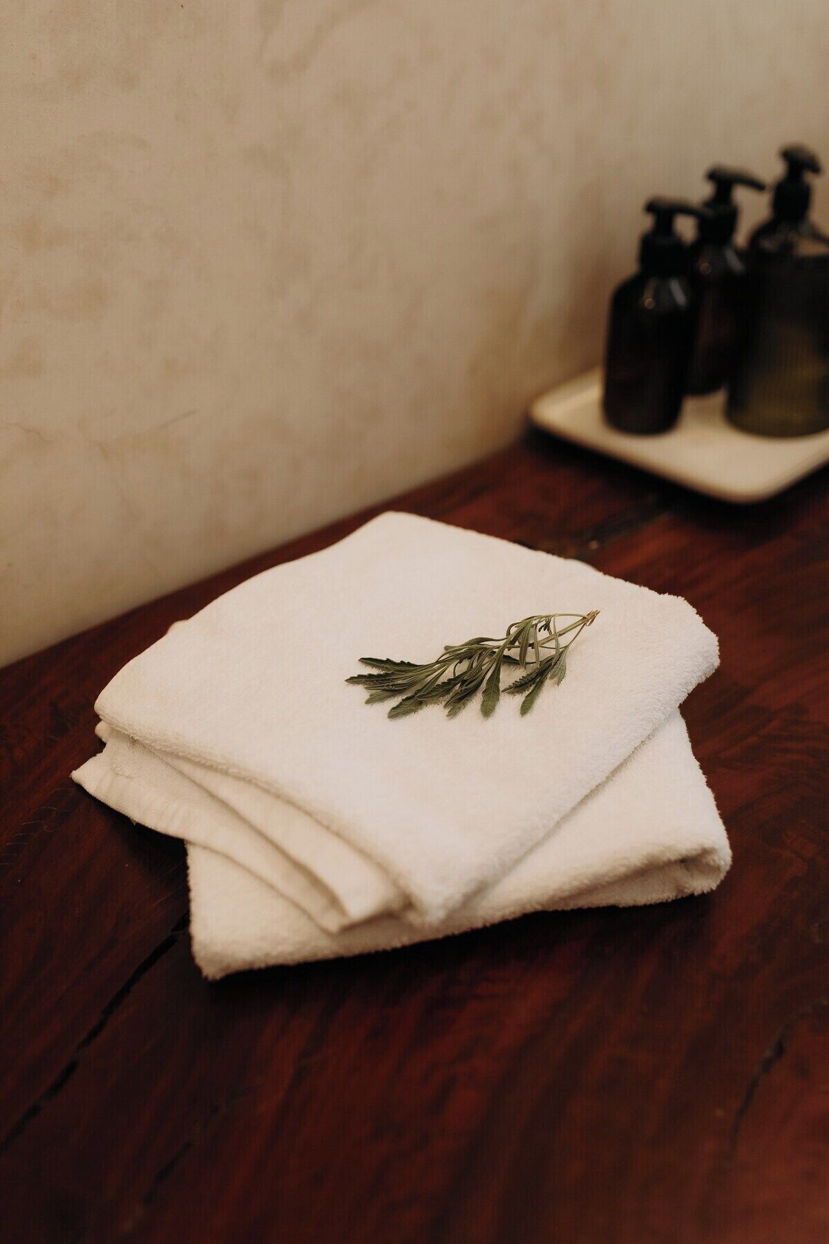 A stack of white towels with a sprig of rosemary on top, placed on a wooden table.